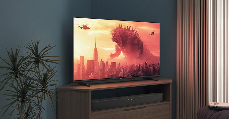 Un televizor Philips pe un suport de colț afișează un film cu Godzilla
