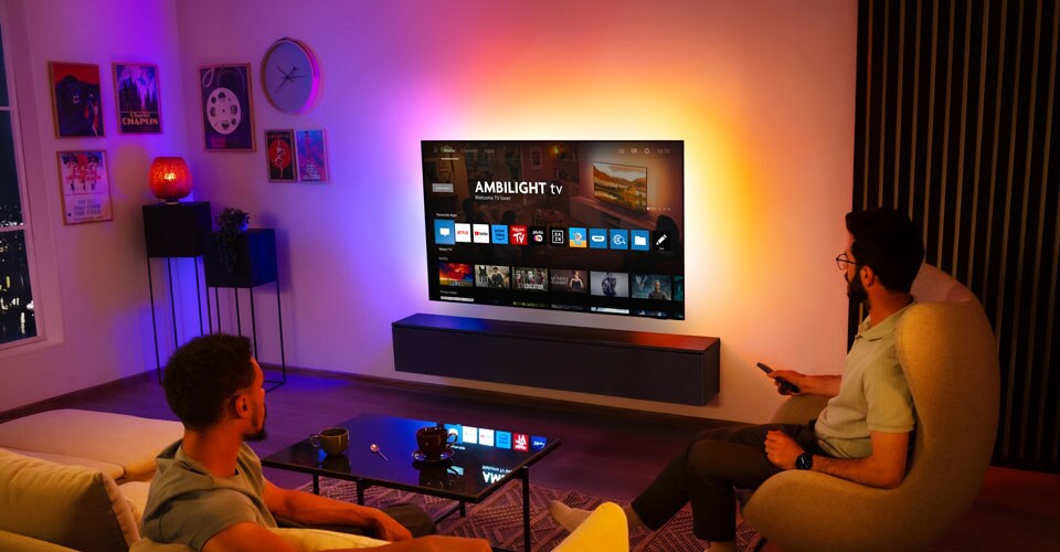 Doi bărbați privesc un televizor Ambilight montat pe perete într-un living