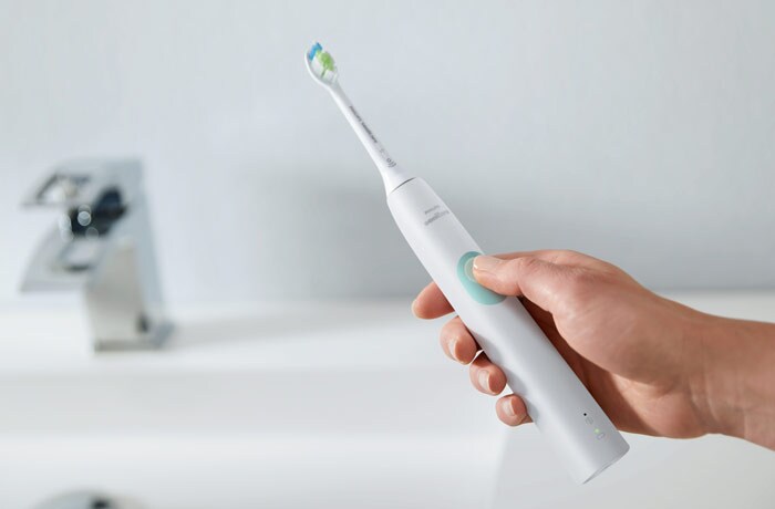 Cineva ține în mână o periuță de dinți electrică Philips Sonicare de culoare albă.