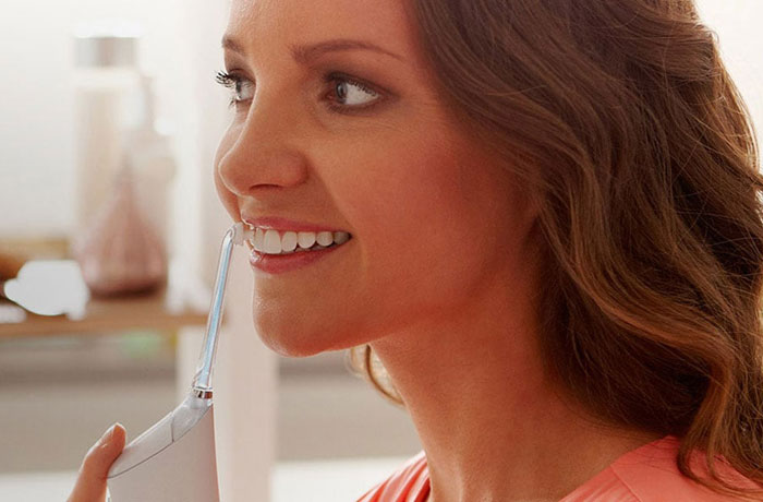 O femeie își periază dinții alb sidefat cu periuța de dinți electrică Philips Sonicare Airfloss. 
