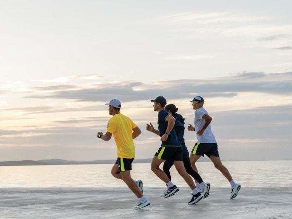 Patru participanţi la alergare aleargă împreună pe plajă.