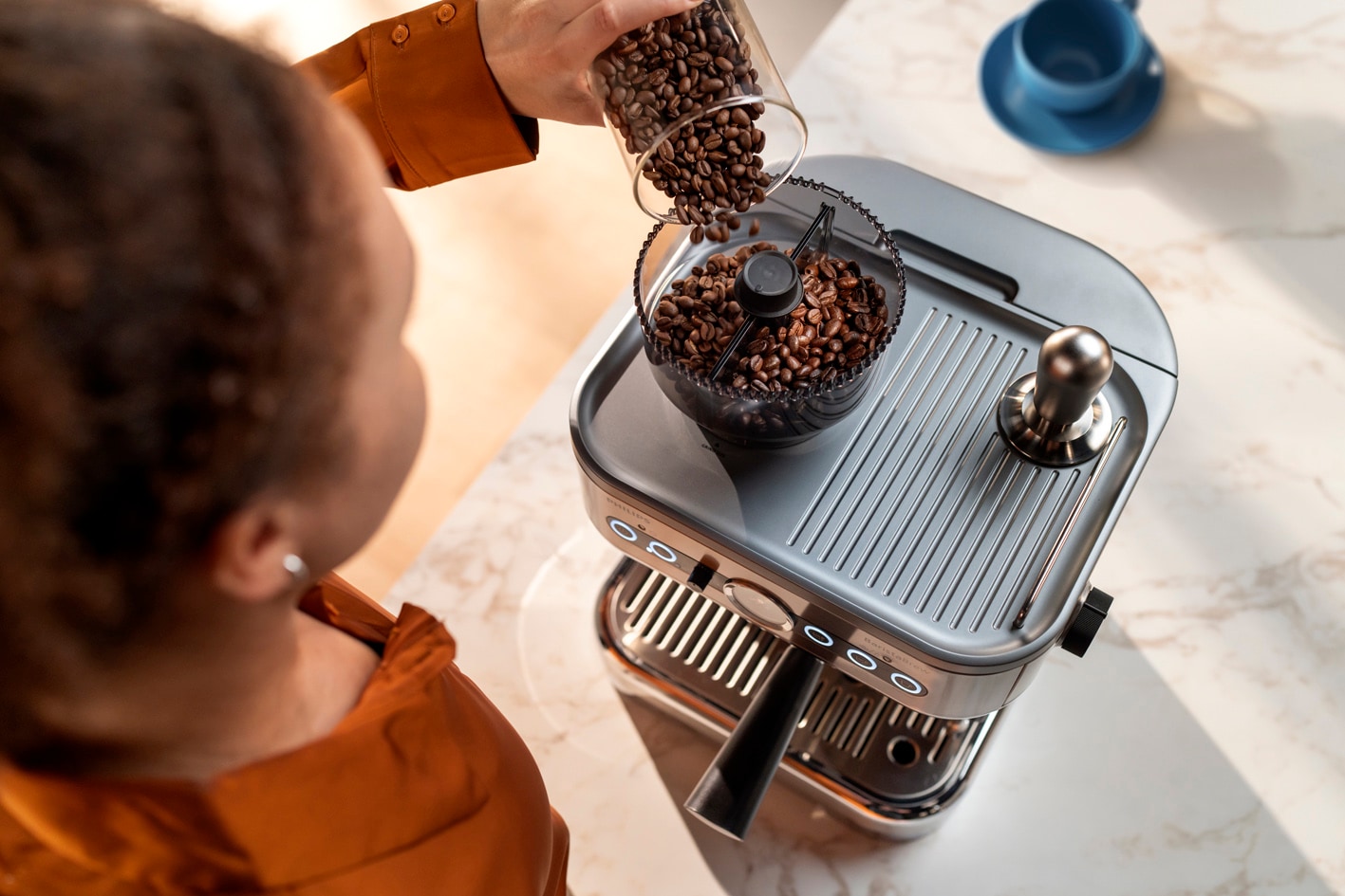 O femeie tânără toarnă cafea boabe în recipientul pentru cafea boabe Philips Barista Brew
